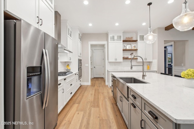 kitchen with appliances with stainless steel finishes, white cabinetry, hanging light fixtures, light stone counters, and wall chimney exhaust hood