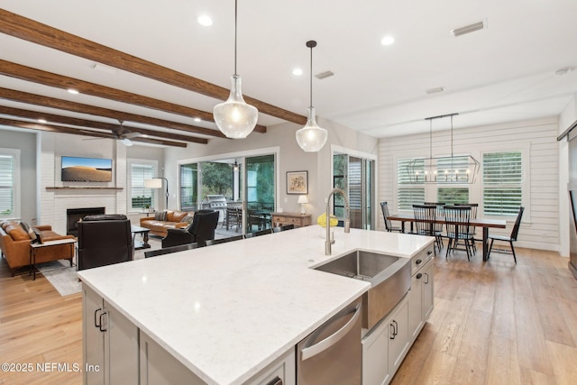 kitchen with sink, a center island with sink, pendant lighting, beam ceiling, and light stone countertops