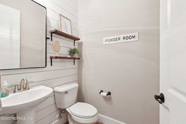 bathroom featuring sink, wood walls, and toilet