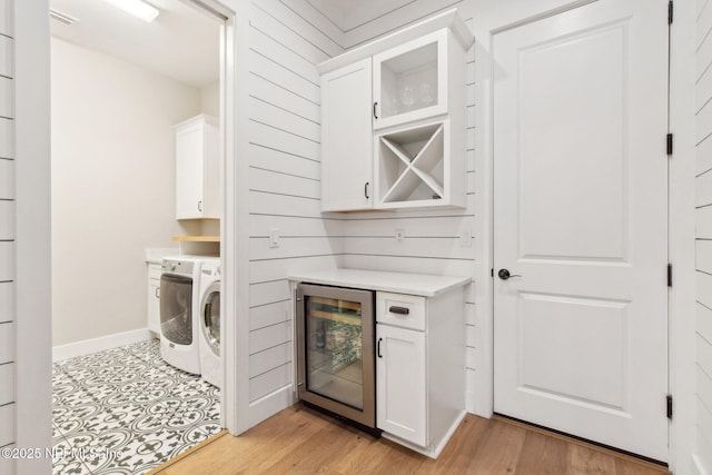 clothes washing area featuring separate washer and dryer, beverage cooler, cabinets, and light wood-type flooring