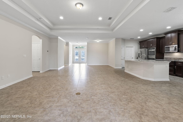 kitchen with dark brown cabinetry, stainless steel appliances, a raised ceiling, and a kitchen island with sink