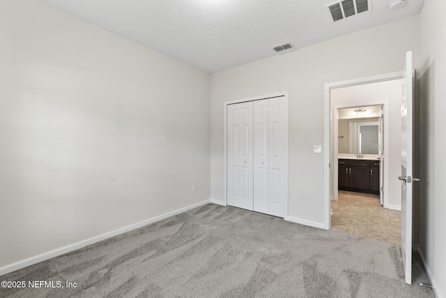 unfurnished bedroom with sink, light colored carpet, a textured ceiling, and a closet