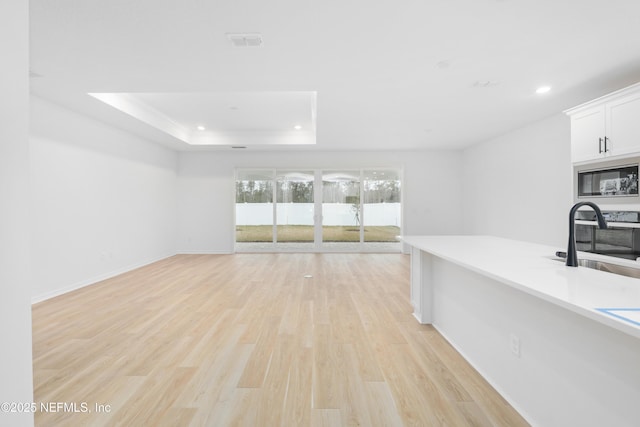 interior space with sink, light hardwood / wood-style flooring, and a raised ceiling