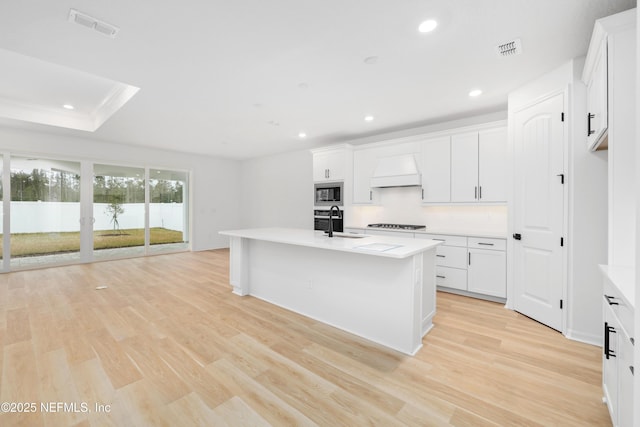 kitchen featuring custom exhaust hood, white cabinetry, a center island with sink, and stainless steel microwave