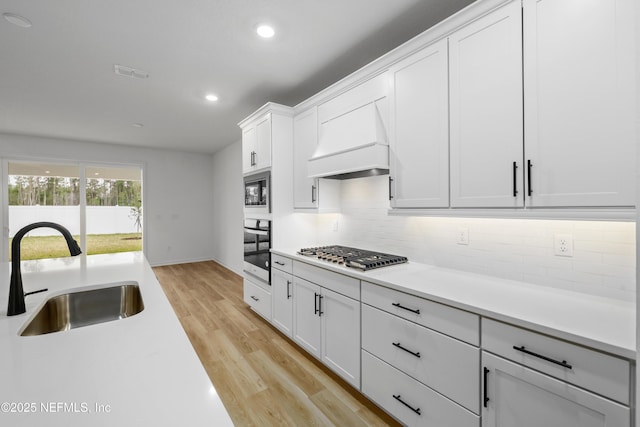 kitchen featuring appliances with stainless steel finishes, sink, white cabinets, custom range hood, and light wood-type flooring