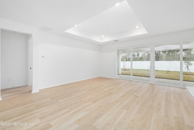 empty room featuring a tray ceiling and light wood-type flooring