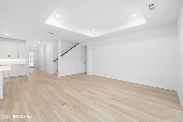 unfurnished living room with ornamental molding, light hardwood / wood-style floors, and a tray ceiling