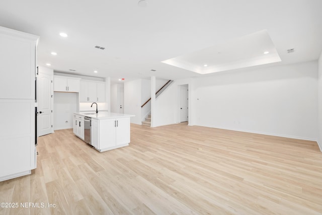 kitchen with white cabinetry, stainless steel dishwasher, light hardwood / wood-style floors, a raised ceiling, and a center island with sink