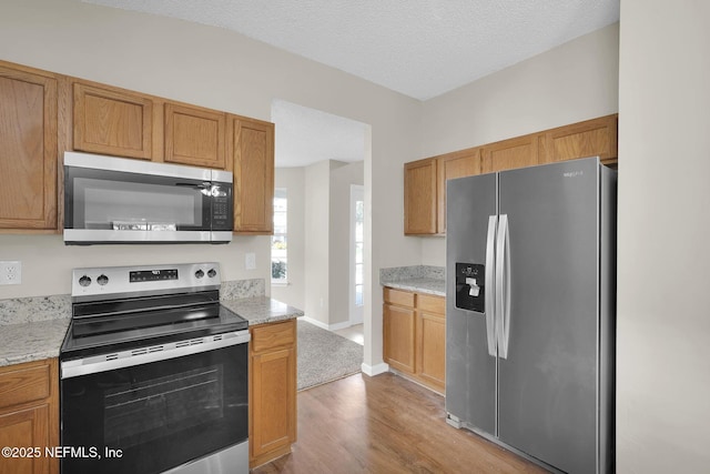 kitchen with light stone countertops, light hardwood / wood-style flooring, stainless steel appliances, and a textured ceiling