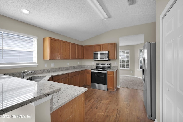 kitchen featuring sink, stainless steel appliances, light hardwood / wood-style floors, vaulted ceiling, and kitchen peninsula