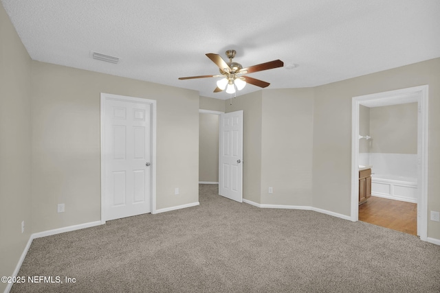 unfurnished bedroom with ceiling fan, ensuite bathroom, carpet floors, and a textured ceiling