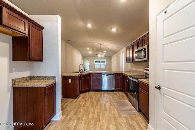 kitchen featuring kitchen peninsula, appliances with stainless steel finishes, light wood-type flooring, a chandelier, and lofted ceiling