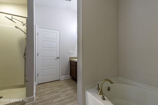 bathroom with vanity, hardwood / wood-style floors, a tub to relax in, and lofted ceiling