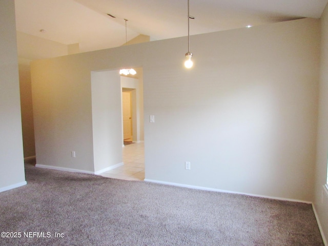 empty room featuring lofted ceiling, light colored carpet, and baseboards