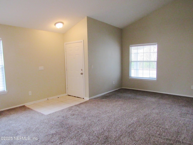 tiled spare room featuring lofted ceiling, carpet flooring, and baseboards