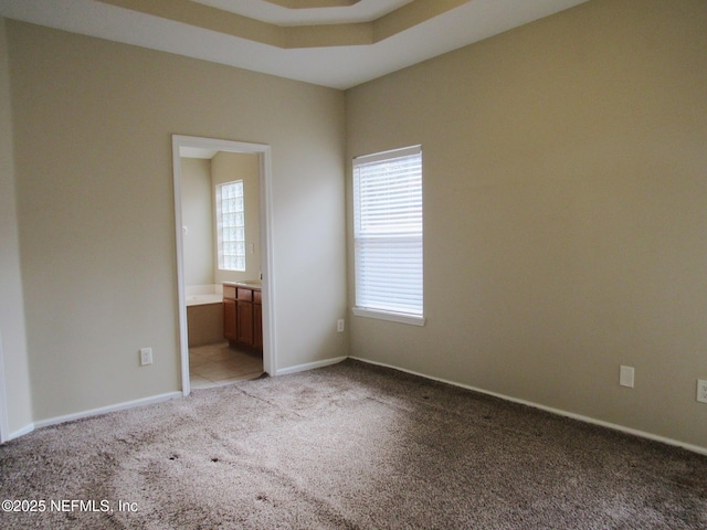 unfurnished room with light carpet, a tray ceiling, and baseboards