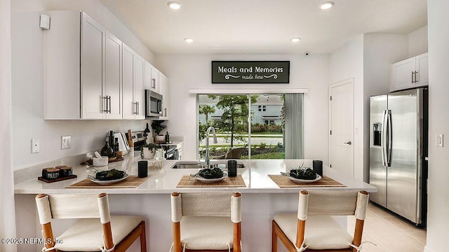 kitchen featuring appliances with stainless steel finishes, white cabinetry, sink, kitchen peninsula, and a breakfast bar area