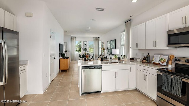 kitchen with kitchen peninsula, sink, white cabinetry, light tile patterned floors, and stainless steel appliances