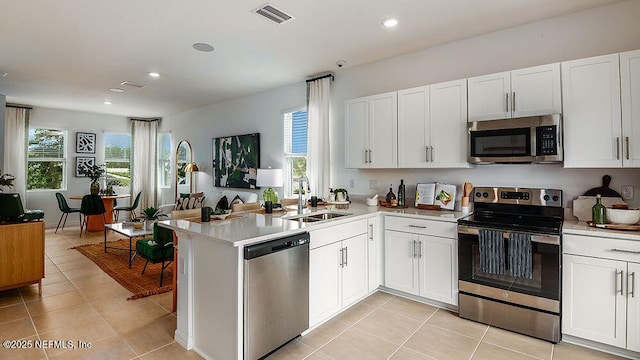 kitchen with appliances with stainless steel finishes, white cabinetry, sink, kitchen peninsula, and light tile patterned floors