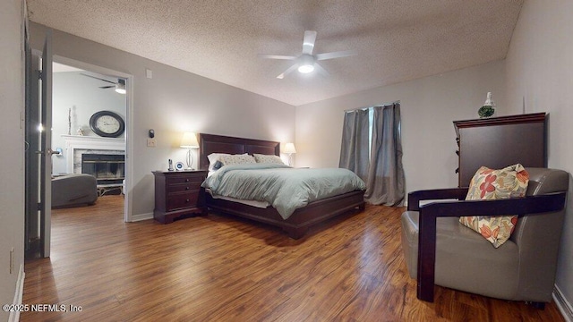 bedroom featuring ceiling fan, wood-type flooring, a high end fireplace, and a textured ceiling