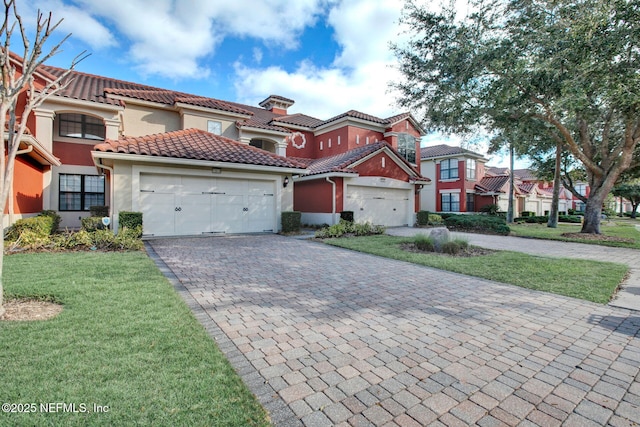 view of front of property with decorative driveway, stucco siding, a front yard, a garage, and a tiled roof