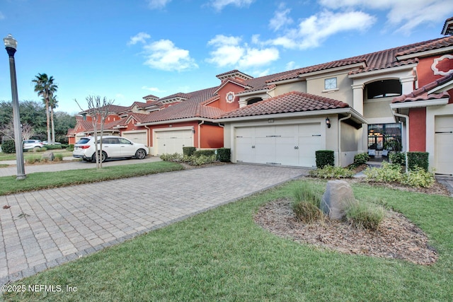 mediterranean / spanish-style house featuring an attached garage, a tile roof, decorative driveway, and stucco siding