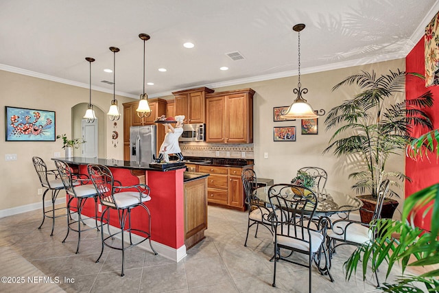 kitchen featuring visible vents, appliances with stainless steel finishes, backsplash, brown cabinetry, and dark countertops