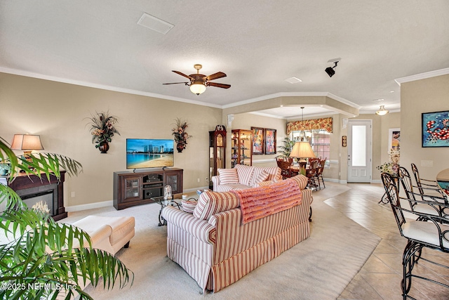 living room with light tile patterned floors, baseboards, a glass covered fireplace, crown molding, and ceiling fan with notable chandelier