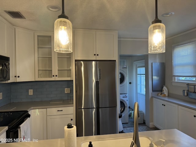 kitchen with black appliances, white cabinets, and stacked washing maching and dryer