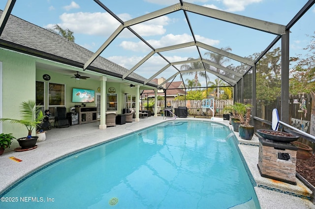 view of swimming pool with pool water feature, glass enclosure, ceiling fan, an outdoor living space, and a patio