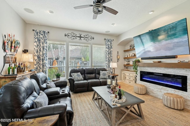 living room with ceiling fan, a fireplace, and a textured ceiling