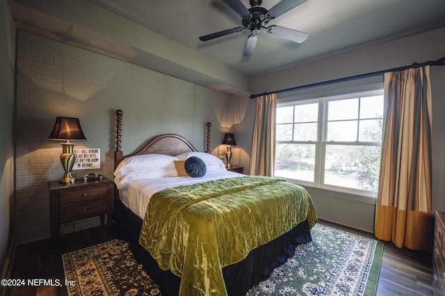 bedroom with ceiling fan, dark wood-type flooring, and brick wall