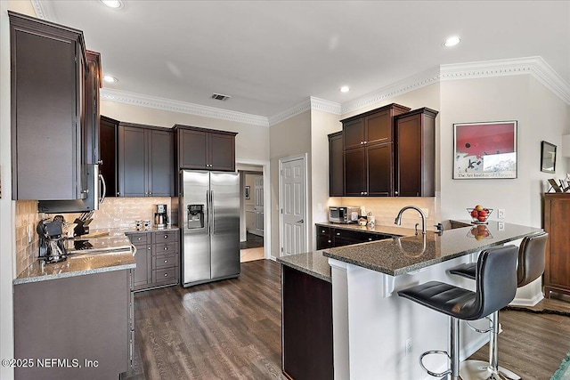 kitchen with appliances with stainless steel finishes, tasteful backsplash, a kitchen breakfast bar, kitchen peninsula, and dark hardwood / wood-style flooring