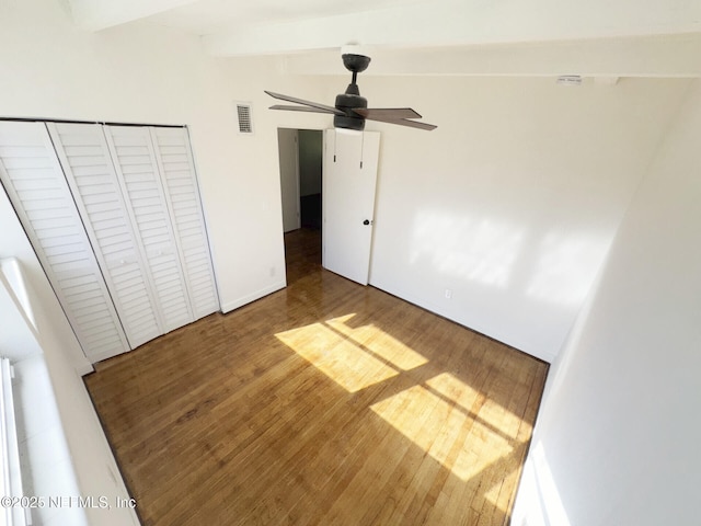 unfurnished bedroom with ceiling fan, hardwood / wood-style floors, a closet, and beam ceiling