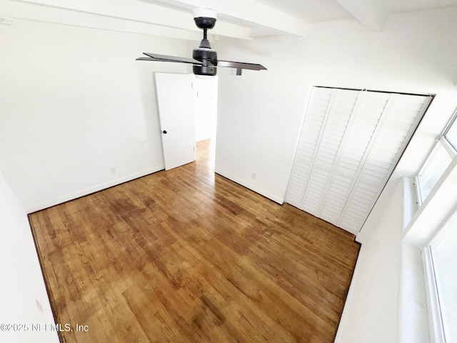 unfurnished bedroom featuring a closet, ceiling fan, beamed ceiling, and wood-type flooring