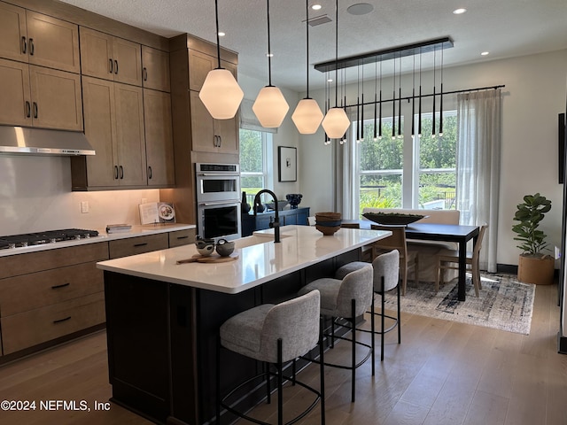 kitchen featuring pendant lighting, dark wood-type flooring, a breakfast bar, an island with sink, and stainless steel appliances