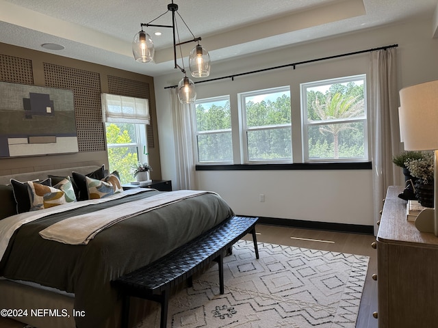 bedroom with hardwood / wood-style flooring, a textured ceiling, multiple windows, and a tray ceiling