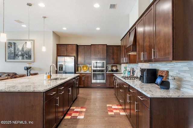 kitchen featuring sink, custom exhaust hood, decorative light fixtures, stainless steel appliances, and decorative backsplash