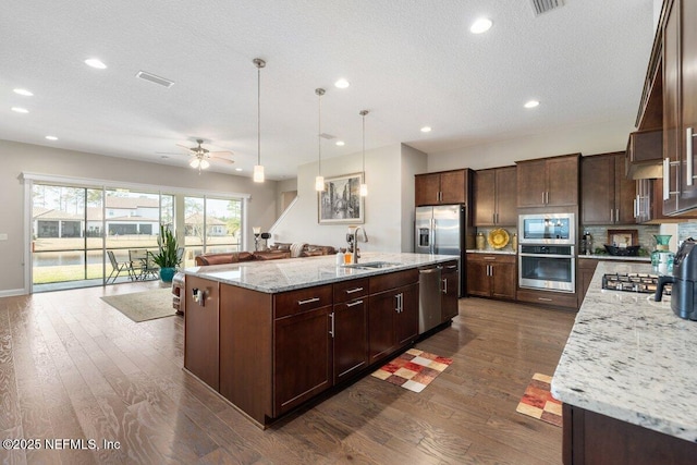 kitchen featuring sink, a large island with sink, light stone counters, stainless steel appliances, and a textured ceiling