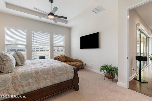 carpeted bedroom with multiple windows, a tray ceiling, and ceiling fan