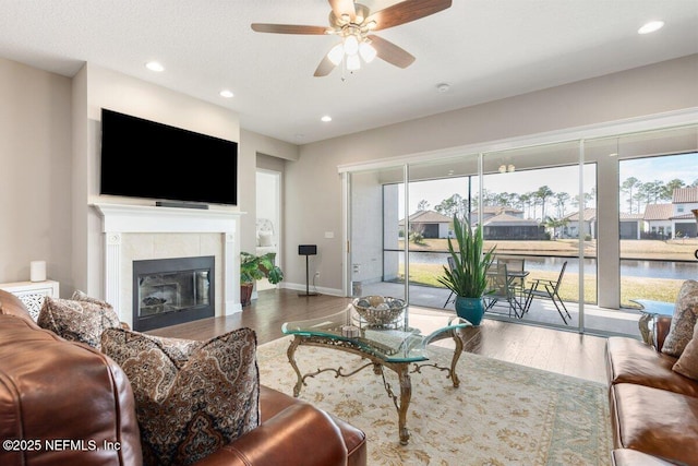 living room featuring a tile fireplace, a water view, hardwood / wood-style floors, and ceiling fan