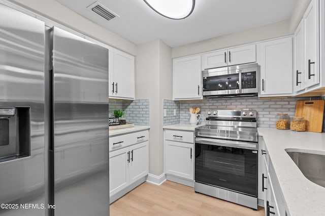 kitchen with tasteful backsplash, white cabinetry, light stone counters, light hardwood / wood-style floors, and stainless steel appliances