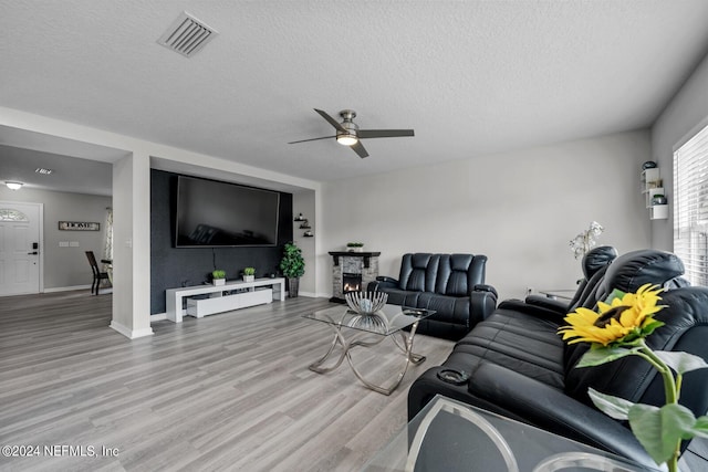 living room featuring a fireplace, light hardwood / wood-style flooring, a textured ceiling, and ceiling fan