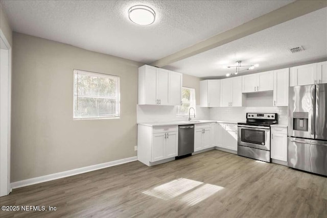 kitchen with light hardwood / wood-style floors, stainless steel appliances, tasteful backsplash, and white cabinets