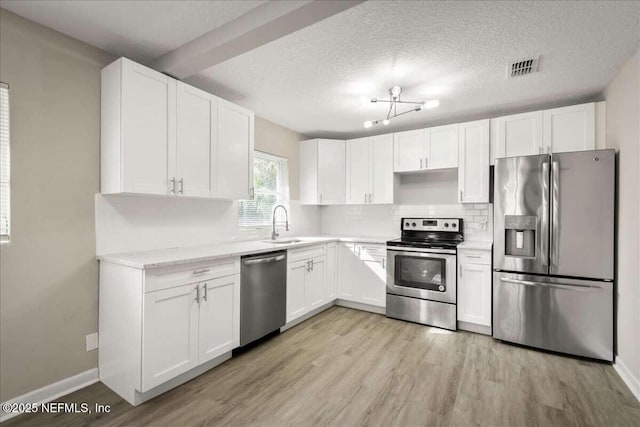 kitchen featuring appliances with stainless steel finishes, light hardwood / wood-style floors, a textured ceiling, and white cabinets