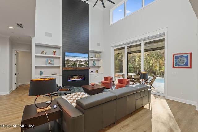 living room featuring crown molding, a fireplace, light hardwood / wood-style floors, and a high ceiling