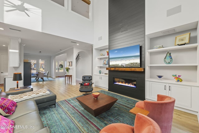 living room with built in shelves, a towering ceiling, a fireplace, and light hardwood / wood-style flooring