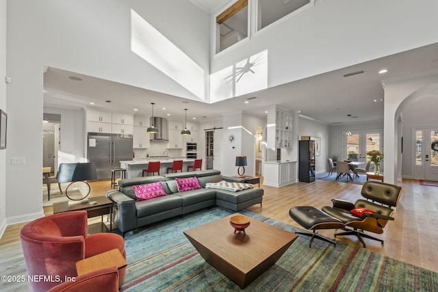 living room featuring crown molding, a towering ceiling, light hardwood / wood-style floors, and french doors