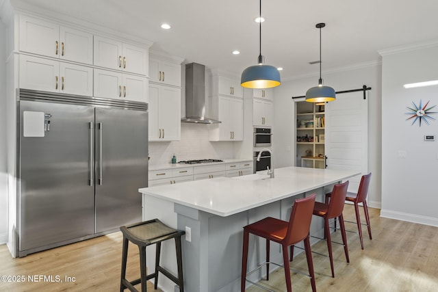 kitchen featuring white cabinetry, a kitchen island with sink, stainless steel appliances, a barn door, and wall chimney exhaust hood