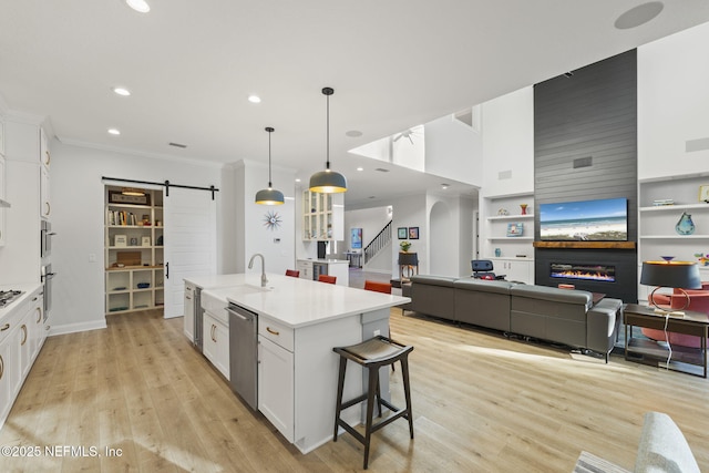 kitchen featuring appliances with stainless steel finishes, decorative light fixtures, white cabinets, a barn door, and a center island with sink